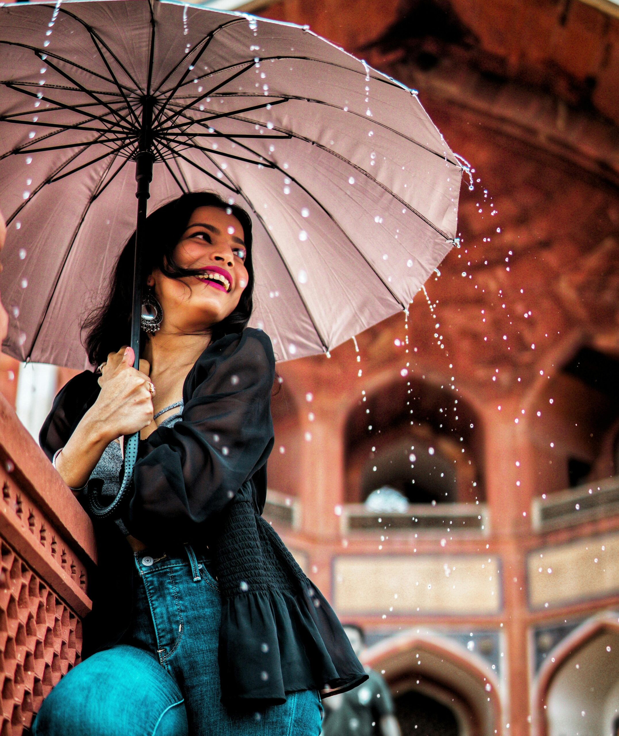 A cheerful woman with an umbrella enjoys the rain in New Delhi's architectural beauty.